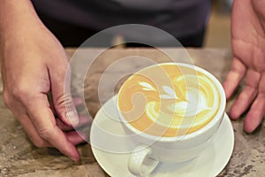 barista hand serve latte coffee in a white coffee cup with heart shape latte art on a vintage wooden table