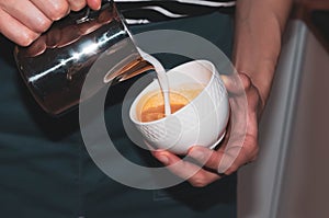 barista hands holding metal jug and white cup and making cappuchino in cafe photo