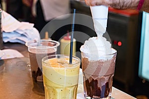 Barista hands pouring cold chantilly cream on a chocolate smoothy on a counter inside a coffee shop