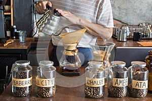 barista holding drip pot and pouring water onto ground coffee beans in the paper filter for brewing drip coffee at the cafe in the