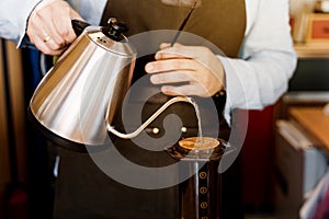 Barista holds kattle in hands and pours hot water in aeropress device with coffee. Alternative method of coffee brewing