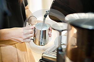 Barista make a cappuccino or latte steaming and frothing milk