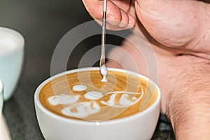 Barista making an art from the fresh milk in the little ceramic cup of the delicious hot espresso