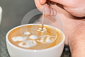 Barista making an art from the fresh milk in the little ceramic cup of the delicious hot espresso