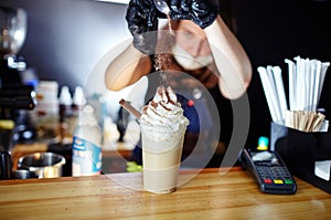Barista making frappe - iced latte coffee with caramel and chocolate syrup and whipped cream