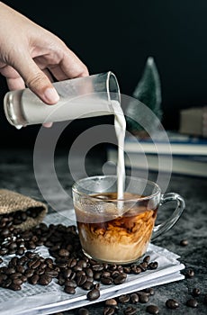 Barista making latte. hand pouring milk into a cup of espresso coffee, preparing coffee drink. vertical image, cropped shot.