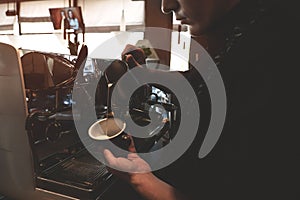 Barista man pouring whipped milk from frothing pitcher in cup with coffee drink standing near professional coffee