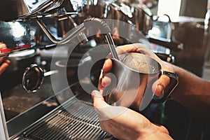 Barista man steaming milk in frothing pitcher using professional coffee machine cappuccinator in cafe