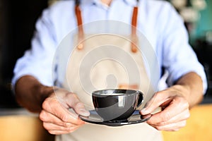 Barista offering a cup of coffee to camera at the coffee shop