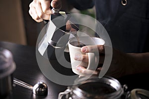 Barista pouring coffee from moka pot coffee maker to a coffee cup. Hand holding Italian classic moka pot pouring coffee