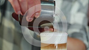 Barista pouring coffee from a silve pot into a glass, perfect glas of latte