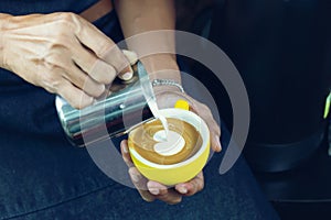 Barista pouring milk foam for making coffee latte art with pattern the heart in a cup