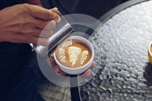 Barista pouring milk foam for making coffee latte art with pattern the leaves in a cup