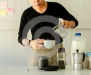 Barista is pouring water in Moka pot coffee into a cup with bottle milk and Brewing equipment on a wooden table