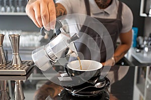 Barista pours coffee from the coffee pot inside contemporary design style cafe with bar