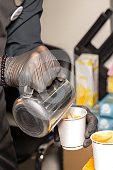 Barista prepares cappuccino by pouring milk into paper cups