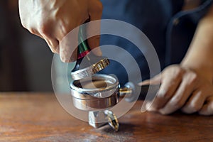 Barista presses ground coffee using tamper, prepares espresso in his coffee shop