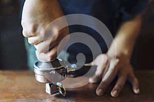 Barista presses ground coffee using tamper, prepares espresso in his coffee shop