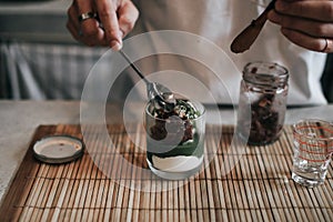 Barista putting red bean and pouring matcha latte from traditional japanese ceramic tool on top vanilla ice cream selective focus