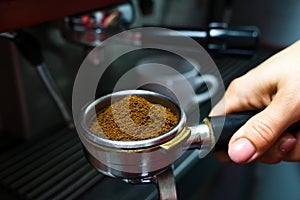 The barista`s hand holds a holder with ground fresh coffee for making coffee in a coffee machine. Close-up. Selective focus