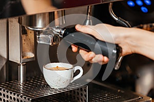 Barista`s hand pours brewed fresh coffee from the coffee machine into a white cup