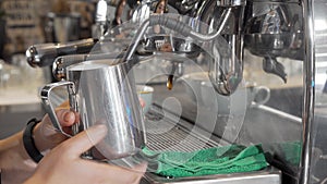 Barista steaming milk in frothing pitcher preparing drinks for coffee shop customers