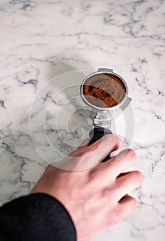 Barista tampering ground coffee in portafilter using tamper. Close-up top view of fresh coffee tablet. Selective focus