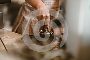 Barista using a tamper to press ground coffee into a portafilter. Coffee maker concept