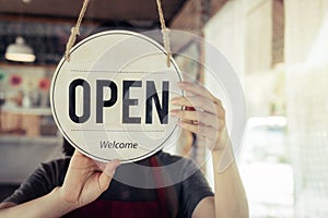 Barista or waitress woman turning open sign board on glass door in modern cafe