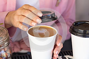 Barista woman closes a mug with a coffee lid