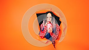 Barmaid with drink looking through hole in paper background. Female bartender with dreadlocks and cup of sweet beverage