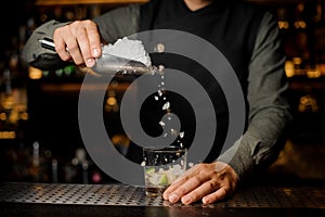 Barman adding ice into the glass with a cane sugar and lime