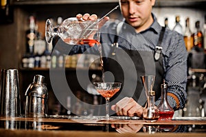 Barman adding red alcoholic drink into the cocktail glass