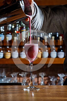 The barman in the bar pours an alcoholic cocktail into a glass with a powerful stream, not afraid to spill on the table