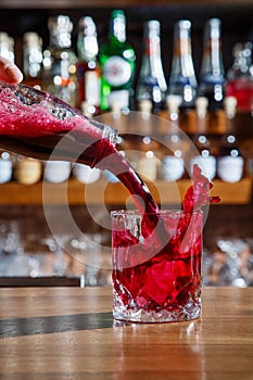 The barman in the bar pours an alcoholic cocktail into a glass with a powerful stream, not afraid to spill on the table