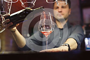 Barman, bartender, male bar attendant pouring wine.