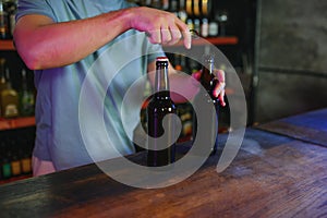 Barman bottle of beer. Nearby empty glass on wooden bar counter in interior of pub, cropped, free space.