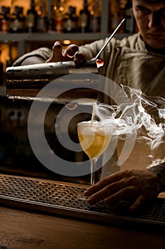 Barman carefully pouring steaming drink from shaker cup into wine glass