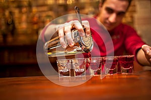 Barman with cocktail shaker pouring red alcoholic drink