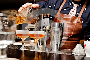 Barman completes the preparation of two alcoholic cocktails using bar equipment