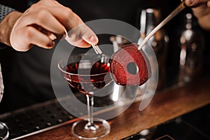 Barman decorating a red cocktail drink with a slice of a beet