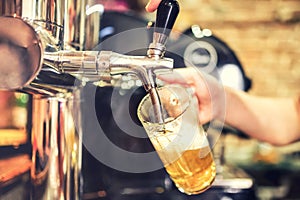 Barman hand at beer tap pouring a draught lager beer serving in a restaurant