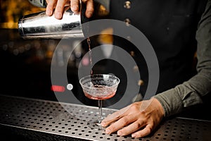 Barman hand pouring alcoholic drink with campari into the cocktail glass