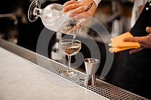 Barman hand pouring alcoholic drink mixed with ice into a glass