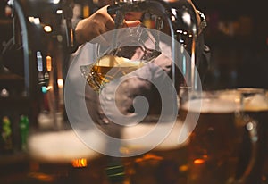 The barman with the help of a tap pours a mug of cold and refreshing light beer