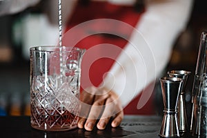 Barman holding a long spoon and glass filled with ice cubes on the bar counter