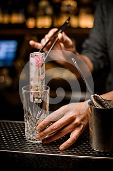 barman holds piece of ice with tongs and puts it into crystal glass on bar counter