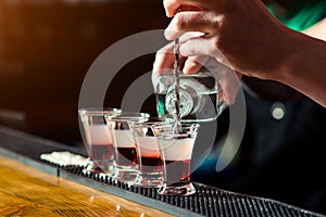 Barman make alcoholic shots in nightclub. Strong alcoholic drink. Multicolored shots on the bar. Small glasses with alcoholic