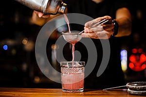 Barman poured an alcoholic cocktail from the shaker into a crystal glass