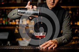 Barman pouring alcoholic drink with campari from shaker into the cocktail glass